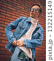 Stylish man adjusting denim jacket in city street with brick wall background 132215149