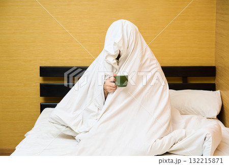 Man wrapping in blanket sitting with cup of coffee in bed 132215871