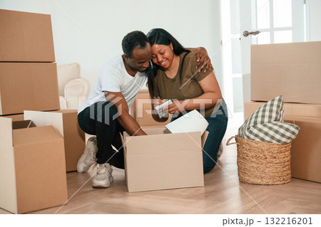 Excited people sitting by the boxes. African American couple are moving into new house 132216201