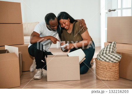 Excited people sitting by the boxes. African American couple are moving into new house 132216203