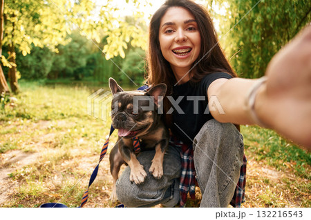 Hand holding camera, doing selfie. Young pretty woman is with her dog in the park 132216543