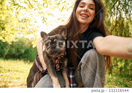 Hand holding camera, doing selfie. Young pretty woman is with her dog in the park Hand holding camera, doing selfie. Young pretty woman is with her dog in the park 132216544