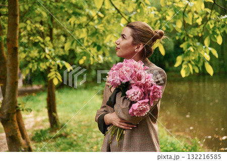 Conception of gift of present. Beautiful young woman is with peonies flowers in the park 132216585
