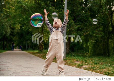 Little boy playing and chasing bubbles in the park 132216586