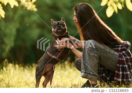 Sitting on the grass, embracing an animal. Young pretty woman is with her dog in the park 132216693