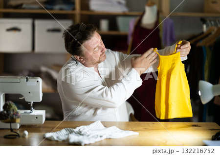 Middle-aged male dressmaker reviewing finished child dress 132216752