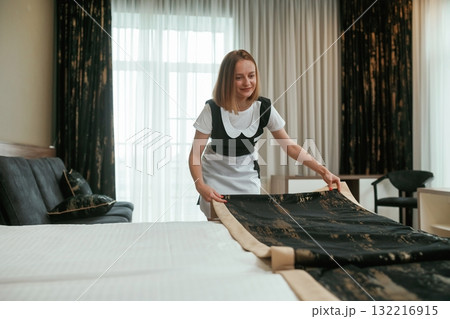 Taking care of bed. Young chambermaid is in hotel room 132216915