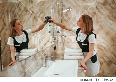 Cleaning the mirror in the bathroom. Young chambermaid is in hotel room Cleaning the mirror in the bathroom. Young chambermaid is in hotel room 132216952