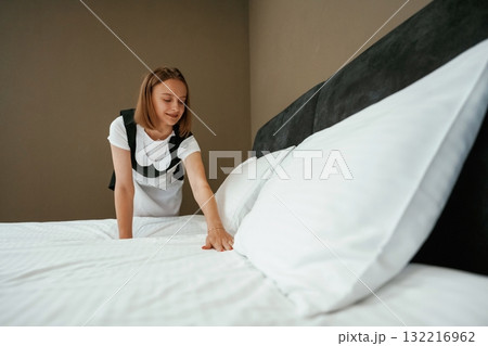 In uniform, taking care of bed. Young chambermaid is in hotel room 132216962