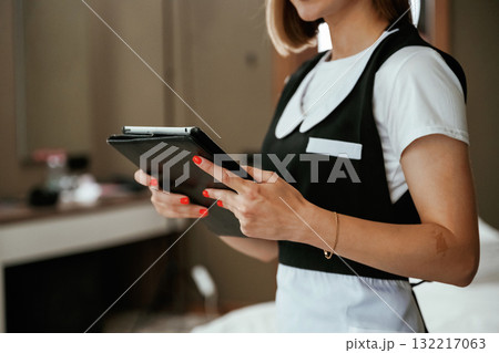 Black digital tablet in hands. Young chambermaid is in hotel room 132217063