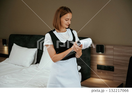 Notepad with documents in hands. Young chambermaid is in hotel room 132217066