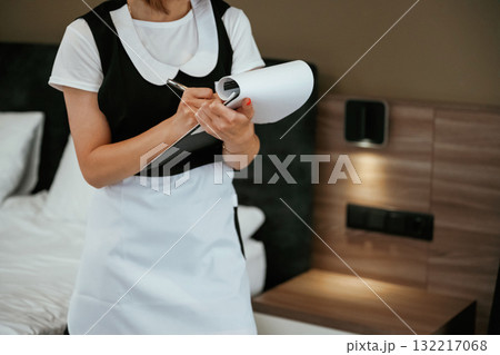 Notepad with documents in hands. Young chambermaid is in hotel room Notepad with documents in hands. Young chambermaid is in hotel room 132217068