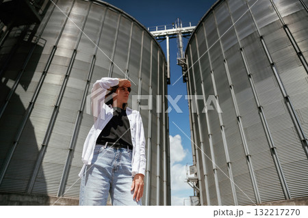 Looking far away. Confident worker standing in front of industrial silos under clear blue sky Looking far away. Confident worker standing in front of industrial silos under clear blue sky 132217270
