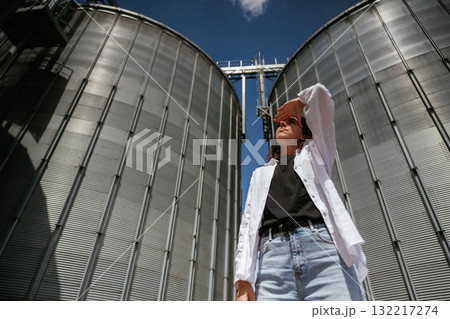 Looking far away. Confident worker standing in front of industrial silos under clear blue sky Looking far away. Confident worker standing in front of industrial silos under clear blue sky 132217274
