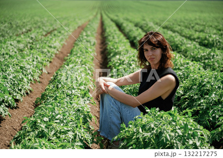 Young woman sitting in lush green field of crops on sunny day 132217275