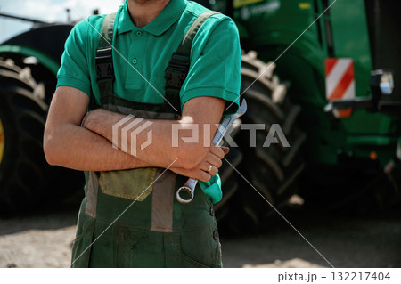 Farmer standing with wrench near a green tractor Farmer standing with wrench near a green tractor 132217404