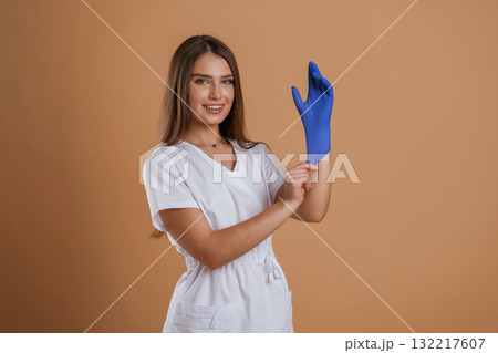 Nurse is wearing the gloves. Young pretty woman is against background in the studio 132217607
