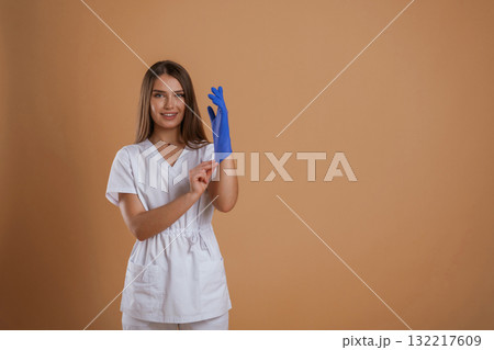 Nurse is wearing the gloves. Young pretty woman is against background in the studio 132217609