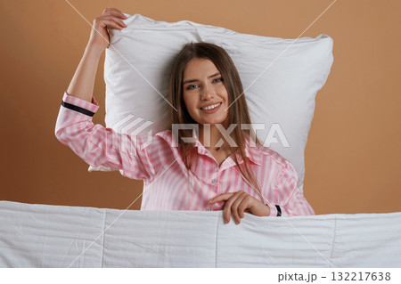 Front view, in pink pajama, waking up. Young pretty woman is against background in the studio Front view, in pink pajama, waking up. Young pretty woman is against background in the studio 132217638