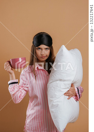 With cup of drink, in pajama and with pillow. Young pretty woman is against background in the studio With cup of drink, in pajama and with pillow. Young pretty woman is against background in the studio 132217641