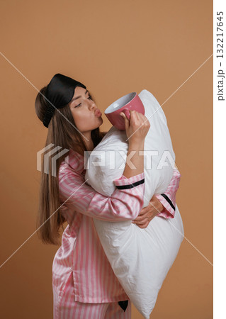Conception of sleep products. With cup and pillow. Young pretty woman is against background in the studio Conception of sleep products. With cup and pillow. Young pretty woman is against background in the studio 132217645