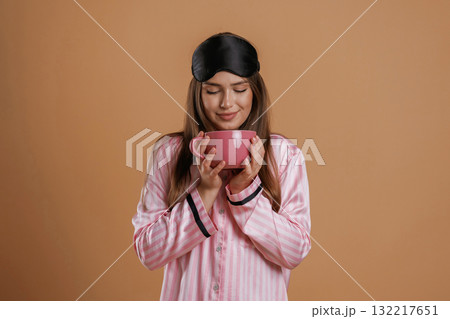 Pink pajama, with cup of drink. Young pretty woman is against background in the studio 132217651