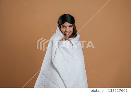 Wrapped in a blanket. Young pretty woman is against background in the studio Wrapped in a blanket. Young pretty woman is against background in the studio 132217661