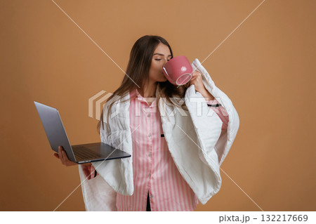 Holding laptop, in sleep clothes. Young pretty woman is against background in the studio 132217669