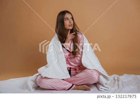 Sitting on the ground, in pajama, morning. Young pretty woman is against background in the studio 132217675