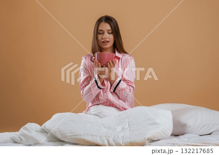 Drinking morning tea, holding cup. Young pretty woman is against background in the studio 132217685