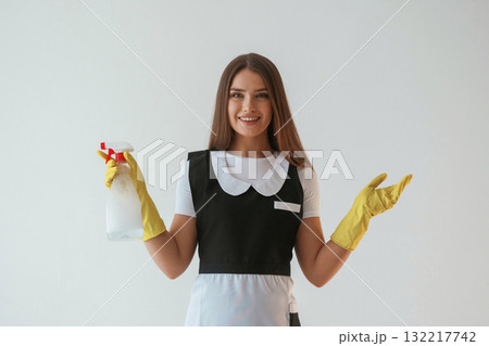 Chambermaid is with cleaning product and tool. Young pretty woman is against background in the studio 132217742