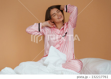 Morning time, in the bed. Young pretty woman is against background in the studio 132217761