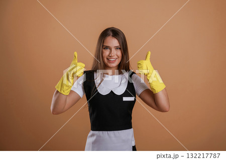Brown backdrop, chambermaid is standing. Young pretty woman is against background in the studio 132217787