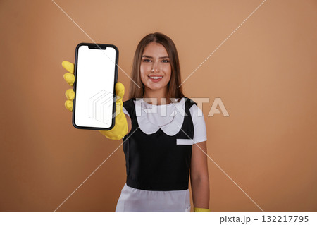 Smartphone with copy space, chambermaid is standing. Young pretty woman is against background in the studio 132217795