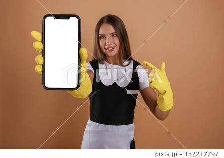 Smartphone with copy space, chambermaid is standing. Young pretty woman is against background in the studio Smartphone with copy space, chambermaid is standing. Young pretty woman is against background in the studio 132217797