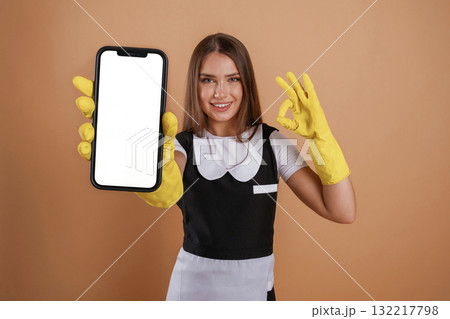 Smartphone with copy space, chambermaid is standing. Young pretty woman is against background in the studio 132217798