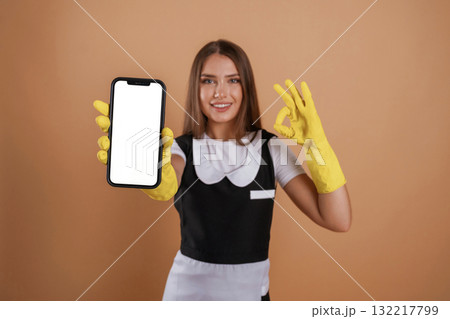 White copy space on smartphone, chambermaid is holding it. Young pretty woman is against background in the studio White copy space on smartphone, chambermaid is holding it. Young pretty woman is against background in the studio 132217799