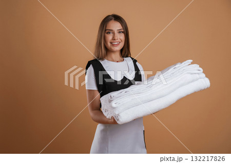 Fresh and clean towels in hands of chambermaid. Young pretty woman is against background in the studio 132217826