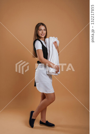View from the side, chambermaid is with new towels. Young pretty woman is against background in the studio View from the side, chambermaid is with new towels. Young pretty woman is against background in the studio 132217855