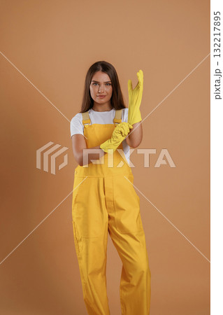 Professional wear, in yellow gloves. Young pretty woman is against background in the studio Professional wear, in yellow gloves. Young pretty woman is against background in the studio 132217895