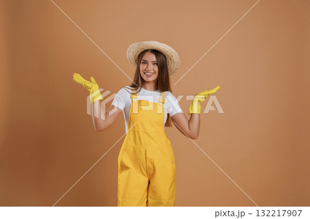 Great look, gardener is in straw hat and yellow uniform. Young pretty woman is against background in the studio 132217907