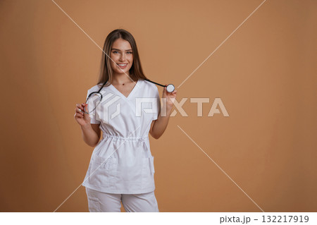 Beautiful nurse is with stethoscope. Young pretty woman is against background in the studio 132217919