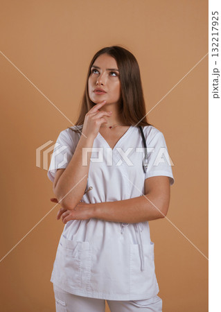In doctor coat, with stethoscope. Young pretty woman is against background in the studio In doctor coat, with stethoscope. Young pretty woman is against background in the studio 132217925