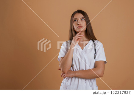 Pretty nurse is in white clothes. Young woman is against background in the studio Pretty nurse is in white clothes. Young woman is against background in the studio 132217927