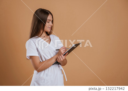 Black notepad in nurse hands. Young pretty woman is against background in the studio Black notepad in nurse hands. Young pretty woman is against background in the studio 132217942