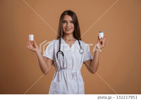 Pills in hands of doctor or a nurse. Young pretty woman is against background in the studio Pills in hands of doctor or a nurse. Young pretty woman is against background in the studio 132217951