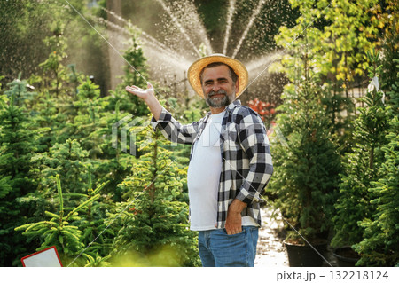 Automatic watering system behind. Senior gardener is at work at daytime Automatic watering system behind. Senior gardener is at work at daytime 132218124