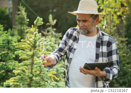Black digital tablet in hand. Senior gardener is at work at daytime Black digital tablet in hand. Senior gardener is at work at daytime 132218167
