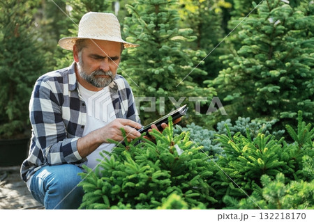 Using digital tablet, sitting. Senior gardener is at work at daytime Using digital tablet, sitting. Senior gardener is at work at daytime 132218170