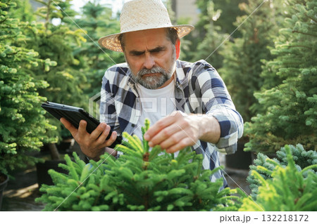Using digital tablet, sitting. Senior gardener is at work at daytime 132218172